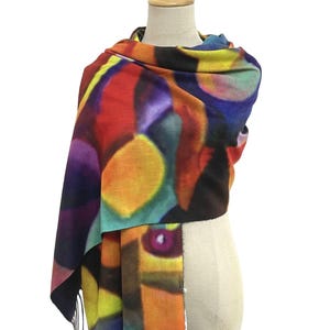 May include: A rectangular scarf featuring an abstract, multi-colored print with bold shapes in shades of red, yellow, blue, purple, and black. The fabric has a soft texture and is finished with thin, straight fringe along the bottom edge.