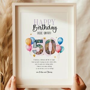 May include: A framed print with the words "HAPPY Birthday LIEBE BIRGIT!" and the number "50" in a watercolor style. Colorful balloons and text are also included. The frame is held by two hands.