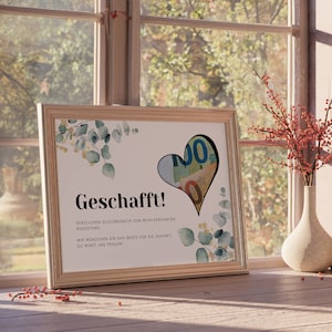 May include: A framed congratulations card with a watercolor design of eucalyptus leaves and a heart-shaped cutout filled with euro bills. The card reads "Geschafft!" which means "Congratulations!" in German. The text below the greeting reads "Herzlichen Gl&uuml;ckwunsch zum wohlverdienten Ruhestand." which means "Congratulations on your well-deserved retirement." The card also includes the text "Wir w&uuml;nschen dir das Beste f&uuml;r die Zukunft. Du wirst uns fehlen!" which means "We wish you all the best for the future. You will be missed!"