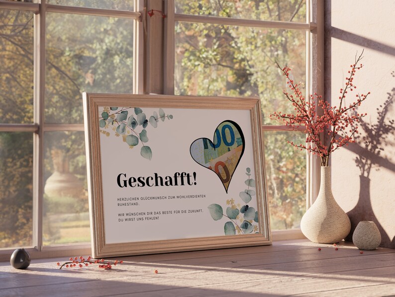 May include: A framed congratulations card with a watercolor design of eucalyptus leaves and a heart-shaped cutout filled with euro bills. The card reads "Geschafft!" which means "Congratulations!" in German. The text below the greeting reads "Herzlichen Gl&uuml;ckwunsch zum wohlverdienten Ruhestand." which means "Congratulations on your well-deserved retirement." The card also includes the text "Wir w&uuml;nschen dir das Beste f&uuml;r die Zukunft. Du wirst uns fehlen!" which means "We wish you all the best for the future. You will be missed!"