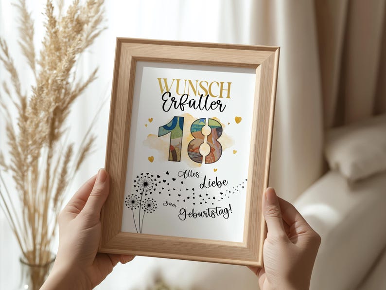 May include: A framed print with the words "Wunsch Erf&uuml;ller 18 Alles Liebe zum Geburtstag!" in gold and black lettering. The number 18 is in a watercolor style. The frame is light brown and is held by two hands.