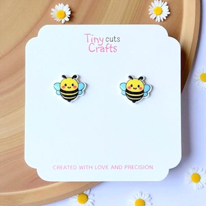 Kawaii bee stud earrings with smiling yellow face, black stripes, blue wings, resin gloss top, white acrylic base, hypoallergenic posts gift for her