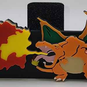 May include: A 3D printed orange and green Charizard Pokemon figurine with a red and yellow flame coming out of its mouth. The figurine is on a black background.