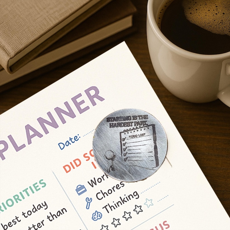 May include: A planner page with the word "PLANNER" in purple, a to-do list, and a metal disc that says "STARTING IS THE HARDEST PART". A white mug of coffee and two notebooks are in the background.
