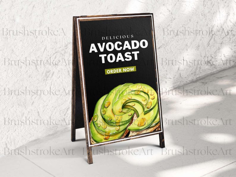 Op de afbeelding: A-frame schoolbordbord met de tekst "Delicious Avocado Toast". Het bord bevat een aquarel illustratie van avocadoschijfjes en de woorden "Order Now". Het bord heeft een donkere achtergrond en een houten frame.