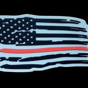 May include: A white, black, and red flag-shaped emblem. The design features the American flag with a red line in the center. The flag has black stripes and a black field of stars. The emblem has a distressed look.