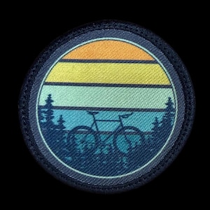 May include: Round patch featuring a bicycle silhouette in front of a forest scene. The top portion has horizontal stripes of orange, yellow, and teal. The patch is bordered by a dark blue stitched edge.