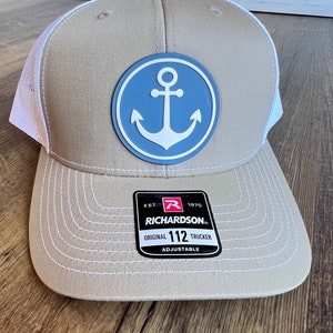 May include: A tan and white trucker hat with a blue anchor patch and the text "EST. 1970 RICHARDSON ORIGINAL 112 TRUCKER ADJUSTABLE" on the back.
