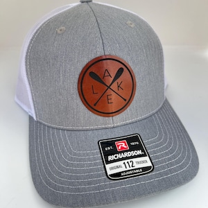 May include: Gray and white trucker hat with a brown leather patch that says "LAKE" with crossed oars. The hat is adjustable and has a Richardson 112 label.