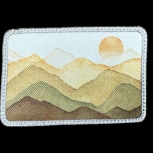 May include: Rectangular patch featuring a watercolor landscape of layered mountains in shades of green, brown, and yellow, with a golden sun in the sky. The patch has a silver stitched border.
