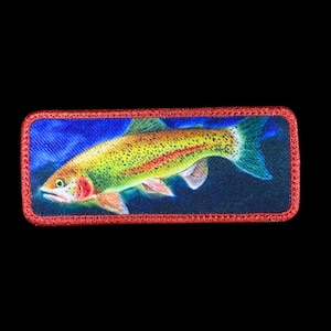 May include: A rectangular patch featuring a colorful fish, likely a trout, with yellow, green, and red hues. The fish is set against a blue background, framed by a red border. The patch is likely an embroidered or printed design.