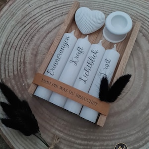 May include: A wooden box with four white candles and a white heart. The candles are labeled "Erinnerungen", "Kraft", "Lichtblick", and "Trost". The box also includes a small white candle holder. The box has a brown paper label that reads "Nimm dir was du brauchst".