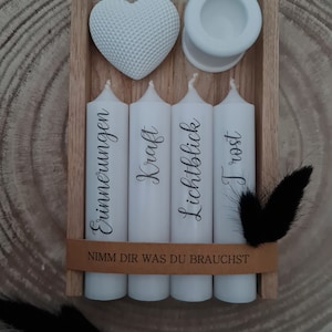 May include: A wooden box with four white candles, each with a different word printed on them: "Erinnerungen", "Kraft", "Lichtblick", and "Trost". The box also includes a white heart and a white candle holder. The text "Nimm dir was du brauchst" is printed on the box.