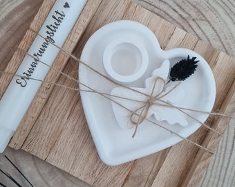 Könnte beinhalten: Weißer Kerzenhalter aus Keramik in Herzform mit einem kleineren herzförmigen Ausschnitt und einem kleinen runden Kerzenhalter im Inneren. Der Kerzenhalter befindet sich auf einem Holztablett mit einer weißen Kerze, auf der "Erinnerungsslicht" steht.