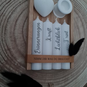 May include: A wooden box with four white candles and a white heart. The candles are labeled "Erinnerungen", "Kraft", "Lichtblick", and "Trost". The box has a brown label that reads "Nimm dir was du brauchst".
