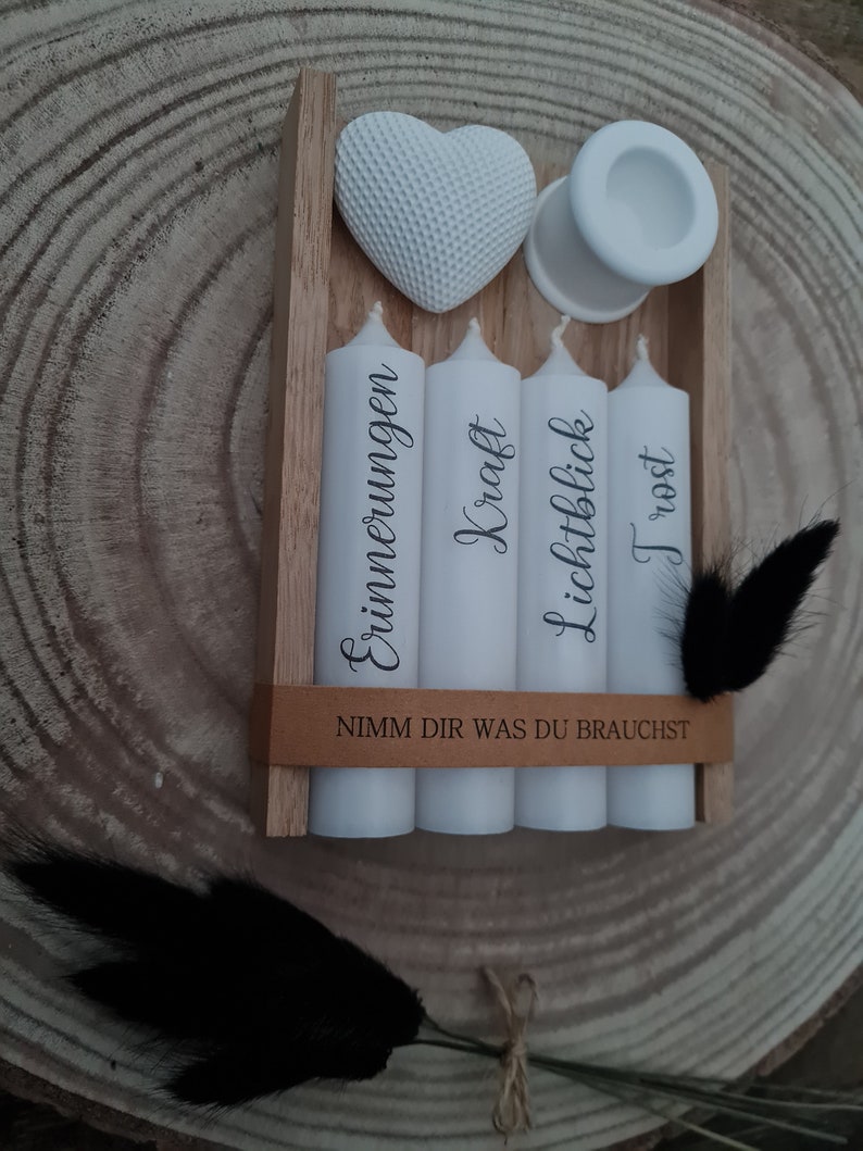 May include: A wooden box with four white candles and a white heart. The candles are labeled "Erinnerungen", "Kraft", "Lichtblick", and "Trost". The box has a brown label that reads "Nimm dir was du brauchst".
