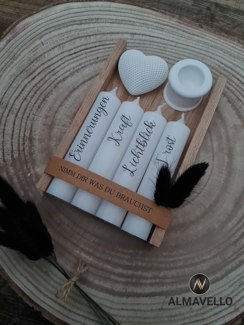 May include: A wooden box with four white candles and a white heart. The candles are labeled "Erinnerungen", "Kraft", "Lichtblick", and "Trost". The box has a brown leather strap with the text "Nimm dir was du brauchst".