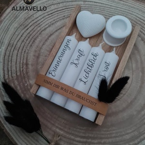 May include: A wooden box with four white candles, each with a different German word written on them. The words are "Erinnerungen", "Kraft", "Lichtblick", and "Trost". The box also includes a white heart and a white candle holder. The text on the box reads "Nimm dir was du brauchst".
