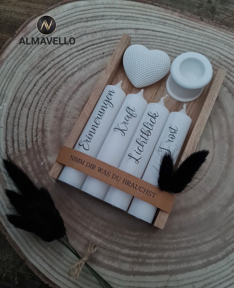 May include: A wooden box with four white candles, each with a different German word written on them. The words are "Erinnerungen", "Kraft", "Lichtblick", and "Trost". The box also includes a white heart and a white candle holder. The text on the box reads "Nimm dir was du brauchst".