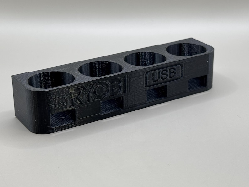 K&ouml;nnte beinhalten: Schwarzer Plastik-Organizer mit f&uuml;nf F&auml;chern zum Aufbewahren von Batterien. Der Organizer tr&auml;gt die Aufschrift "RYOBI" und "USB".