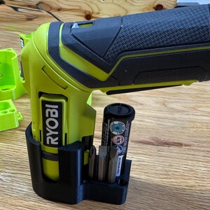 Peut inclure: Un support mural imprim&eacute; en 3D noir et vert pour une perceuse Ryobi avec un porte-batterie et un porte-embouts. La perceuse n'est pas incluse.