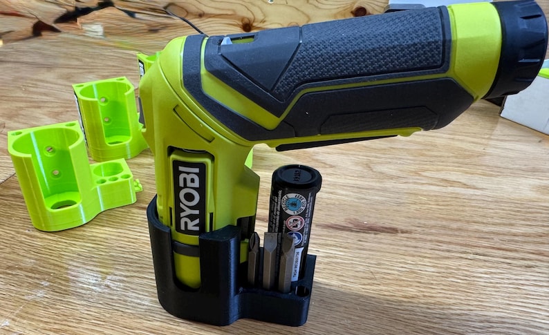 Peut inclure: Un support mural imprim&eacute; en 3D noir et vert pour une perceuse Ryobi avec un porte-batterie et un porte-embouts. La perceuse n'est pas incluse.