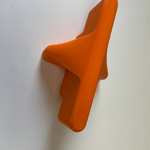 May include: An orange plastic wall mount with a unique design. The mount has a flat base and a curved, angled top.