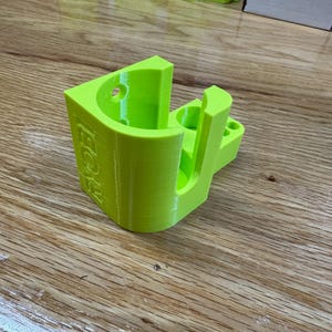 Peut inclure: Un support mural imprim&eacute; en 3D de couleur vert vif avec le mot "BOOST" imprim&eacute; sur le c&ocirc;t&eacute;. Le support a une ouverture circulaire et une fente pour maintenir un objet.