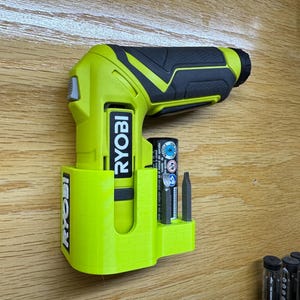 Peut inclure: Une perceuse-visseuse Ryobi verte et noire avec un porte-batterie et un porte-embouts. La perceuse est fix&eacute;e au mur.