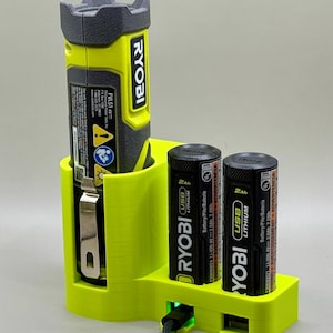May include: A lime green and black Ryobi flashlight and two black Ryobi USB lithium batteries are in a lime green charging station. The flashlight is labeled "FVL51 4V". The batteries are labeled "2Ah USB Lithium".