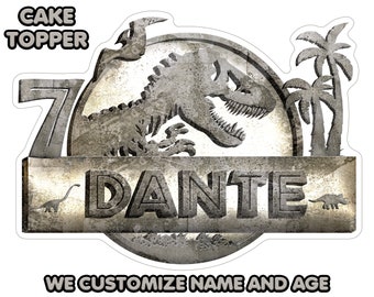 May include: A grey and white cake topper featuring a dinosaur with the text "DANTE" and the number "7". The topper is designed to look like a weathered stone sign with palm trees in the background. The text "WE CUSTOMIZE NAME AND AGE" is at the bottom of the topper.