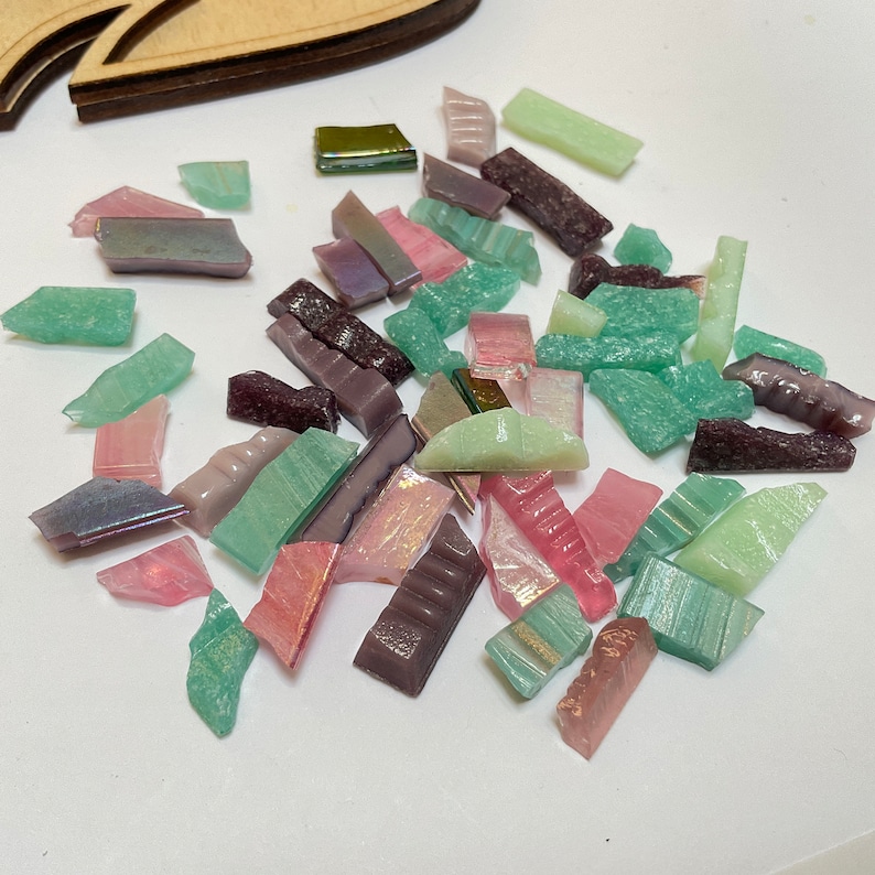 May include: Assortment of small, colorful glass tiles in shades of green, pink, purple, and brown. The tiles are irregular in shape and size, and some have a shimmery finish.