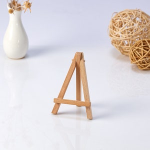 Könnte beinhalten: Ein kleiner Holzstaffelei, perfekt zum Ausstellen von kleinen Kunstwerken oder Fotos. Die Staffelei ist aus Naturholz gefertigt und hat ein schlichtes, klassisches Design.