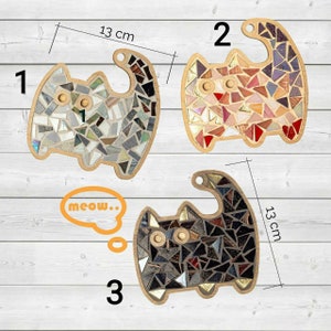 Può includere: Tre ornamenti di gatto in legno, ognuno con un diverso motivo a mosaico. I gatti sono alti 13 cm e hanno un fumetto 'miao' sopra di loro. I gatti sono grigi, rosa e neri.