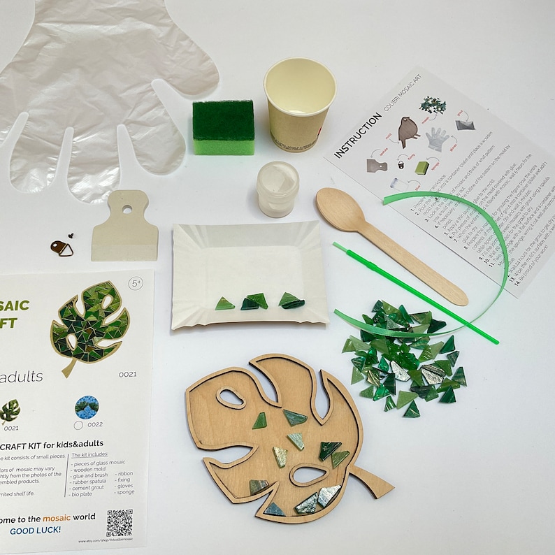 May include: A craft kit for making a mosaic art project. The kit includes a wooden leaf-shaped base, green glass mosaic tiles, glue, a sponge, and instructions. The kit is labeled "CRAFT KIT for kids & adults".