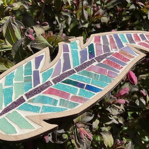 May include: A wooden feather mosaic with a colorful design. The feather is made of small pieces of glass in shades of blue, green, purple, and pink.