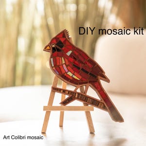 May include: DIY mosaic kit featuring a red cardinal bird on a wooden easel. The cardinal is made of small, colorful glass tiles.