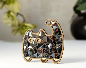 May include: A black cat-shaped wooden ornament with a mosaic design made of small, iridescent triangles. The cat's eyes are outlined in gold.