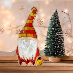 Puede incluir: Decoraci&oacute;n navide&ntilde;a de gnomo de madera con sombrero de mosaico rojo, amarillo y naranja. El gnomo tiene barba de mosaico blanco y abrigo rojo. Un peque&ntilde;o &aacute;rbol de Navidad verde est&aacute; junto al gnomo.
