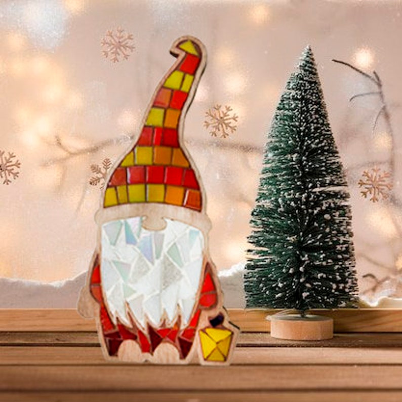 Puede incluir: Decoraci&oacute;n navide&ntilde;a de gnomo de madera con sombrero de mosaico rojo, amarillo y naranja. El gnomo tiene barba de mosaico blanco y abrigo rojo. Un peque&ntilde;o &aacute;rbol de Navidad verde est&aacute; junto al gnomo.