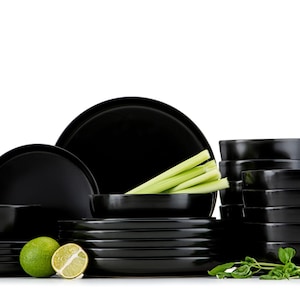 Peut inclure: Un ensemble complet de vaisselle noire, comprenant des assiettes, des bols et des plats de service. L'arrangement comprend du céleri frais et des citrons verts, suggérant un thème de restauration. La finition brillante de la vaisselle contraste avec les produits frais.
