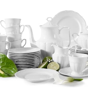 Puede incluir: Un conjunto de vajilla de porcelana blanca, que incluye tazas, platillos, platos, una tetera, una crema y un azucarero. El conjunto está dispuesto con hojas verdes, limas y flores blancas, creando una exhibición elegante.