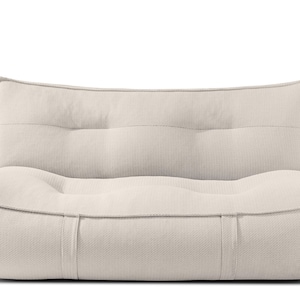 Puede incluir: Un sillón tapizado beige de perfil bajo con asiento redondeado y respaldo ligeramente curvado. La silla tiene una tela texturizada y un diseño minimalista, adecuado para un espacio vital moderno. El respaldo tiene tres botones.