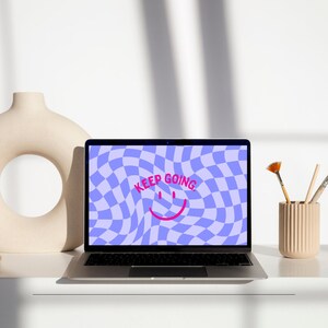 Puede incluir: Un ordenador portátil con un fondo de pantalla a cuadros azules y blancos. El texto "KEEP GOING" se muestra en rosa con una carita sonriente rosa.