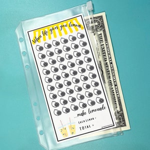 Puede incluir: Una hoja blanca con un diseño de limón en blanco y negro y el texto "When life gives you lemons... make lemonade. Each lemon = TOTAL = ". La hoja está en una bolsa transparente de plástico con cremallera y un billete de dólar visible.