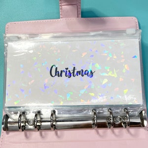 May include: A clear plastic pocket with a white background and iridescent confetti pattern. The pocket is labeled "Christmas" and is inserted into a pink binder.