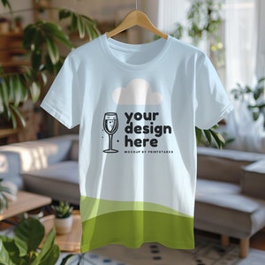 Op de afbeelding: Een lichtblauw t-shirt met een witte wolk en een glas champagne. De tekst "your design here" is op het shirt gedrukt. MOCKUP BY PRINTSTARKS.