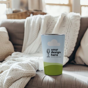 May include: A stainless steel tumbler with a light blue background and a green grass design. The tumbler has a white cloud and a black line drawing of a wine glass with the text "your design here. MOCKUP BY PRINTSTARS".