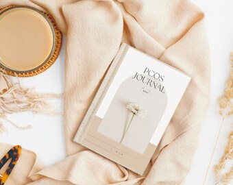 May include: A journal with the text "PCOS JOURNAL" on the cover, featuring a minimalist design with a flower illustration. The journal is set on a beige scarf with a cup of coffee and a hair clip. The overall aesthetic is soft and neutral.
