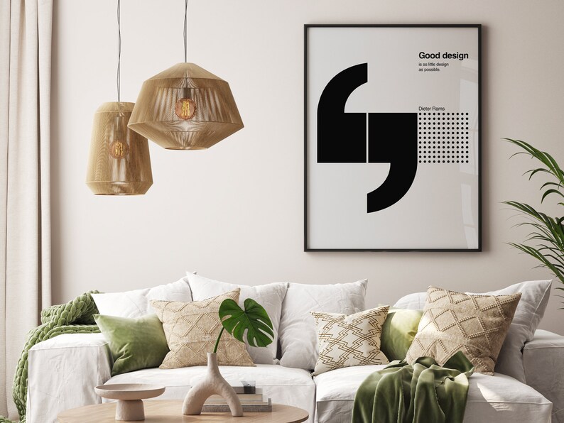May include: A living room interior with a white couch, green throw pillows, and a throw blanket. Two woven pendant lights hang from the ceiling. A framed poster with black text that reads "Good design is as little design as possible" hangs on the wall.